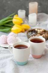 A tasty snack: two cups of tea, a plate of zephyr and a box of sweets.