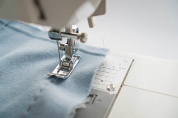 Sewing machine and item of blue clothing. Close-up of skirt sewing and sewing machine mechanism. Sewing machine needle stuck into blue fabric.