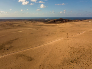 Fototapeta na wymiar Aerial view of a desert landscape on the island of Lanzarote, Canary Islands, Spain. Road that crosses a desert. Reliefs on the horizon. Volcanoes.