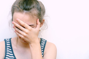 Fototapeta premium Girl in despair covers her face with hand. Stressed woman at home headache pain female portrait. Preaty sad girl close face and head by hand standing alone