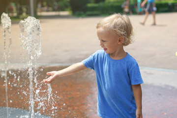 A boy playing with water in park fountain. Hot summer. Happy young boy has fun playing in water fountains