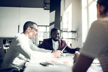Cheerful dark-skinned colleague smiling looking at his secretary