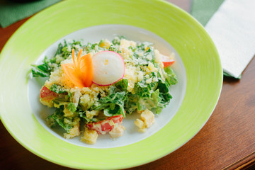 Salad with radish, carrot, lettuce and cheese in a green plate.