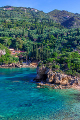 Beautiful landscape with sea, mountains and cliffs, green trees and bushes, rocks in a blue water. Corfu Island, Greece. 