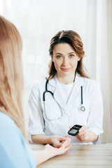 cropped view of donor and doctor measuring glucose level with glucometer