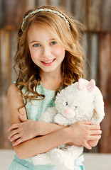 Portrait little cute girl with blond hair in a beautiful dress stay in a bright studio and holding a soft toy.