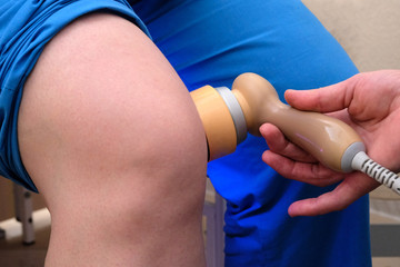 Treatment of kneecaps for the elderly in the hospital. Close-up of the doctor warms the knee of a woman with an electric apparatus. Laser treatment. Healthy joints.