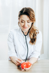 smiling doctor with stethoscope listening plastic heart in clinic