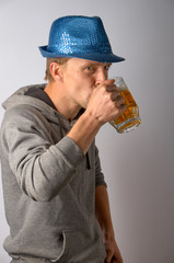 The guy in the blue hat drinks a light cold beer from a transparent mug
