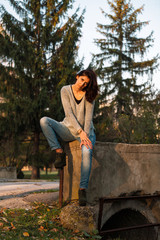 Sexy brunette sits in a defiant pose. Green firs in background.