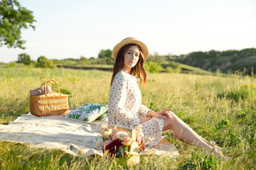 Happy Woman Life Style, beautiful relaxed girl in a straw hat on the nature picnic basket flowers in the rays of the soft sunset sun, a picnic - camping