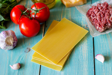 Lasagna, tomatoes, minced meat and other ingredients. Blue wooden background. Italian cuisine.