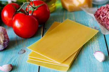 Lasagna, tomatoes, minced meat and other ingredients. Blue wooden background. Italian cuisine.
