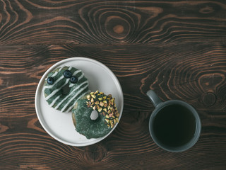 Vegan doughnuts with chia seeds topped with healthy spirulina glaze with pistachio and blueberry. Blue green spirulina donuts and tea cup on brown wooden background, top view or flat lay. Copy space