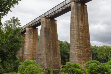 Giant train trestle crossing made of stone blocks over a river with lush green vegetation