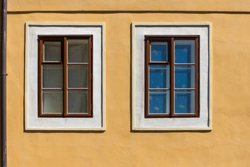 Two wooden brown windows with white trim on amber wall