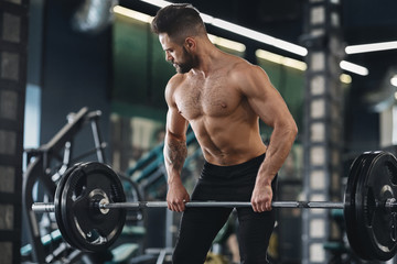 Fototapeta na wymiar Strong weightlifter working out with heavy barbell in gym