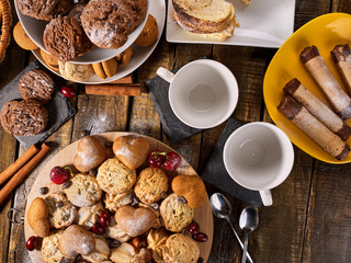 Oatmeal cookies and sand chocolate cake with cherry berry on cutting board on wooden table in rustic style. Top view of still life served with cups and dessert spoons. Increase performance and mood.