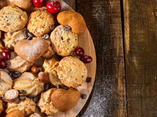 Oatmeal cookies and sand chocolate cake with cherry berry and crispy wafer rolls with cream on cutting board on wooden table in rustic style. Several recipes for baking.