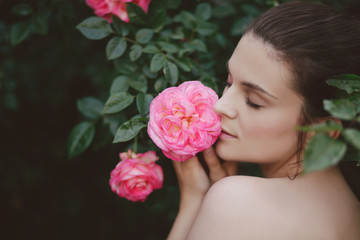 Naklejka premium Young beautiful woman portrait close up with perfect skin posing with pink roses flowers in a garden