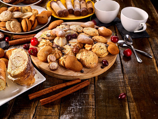 Oatmeal cookies and sand chocolate cake with cherry berry and crispy wafer rolls with cream on cutting board on wooden table in rustic style. Delight pleasant taste.
