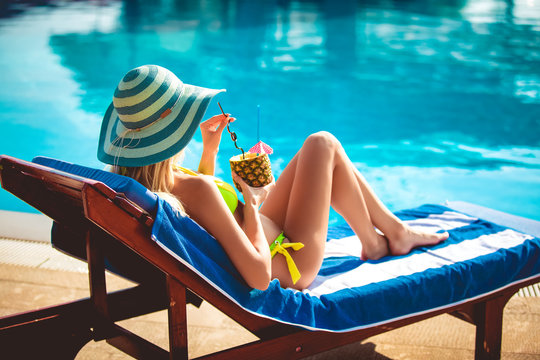 Portrait of young woman with cocktail chilling in the tropical sun near swimming pool on a deck chair