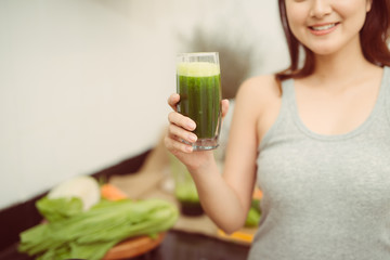 Pretty young woman drinking a vegetable smoothie in her kitchen