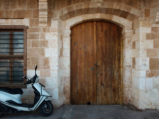 Parked scooter, wooden gates and barred window of antique stone building
