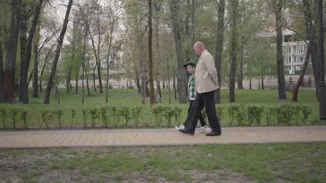 Adorable grandfather and cute little grandson walking in the park together. Generations concept. Friendly family. Leisure outdoors.