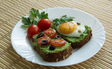 Sandwich with guacamole, egg, olives and tomatoes on a plate