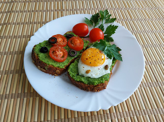 Sandwich with guacamole, egg, olives and tomatoes on a plate