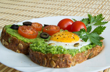 Sandwich with guacamole, egg, olives and tomatoes on a plate