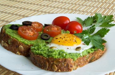 Sandwich with guacamole, egg, olives and tomatoes on a plate