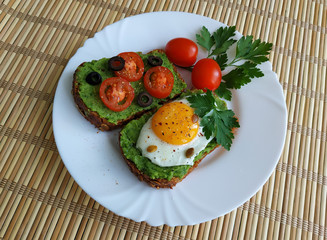 Sandwich with guacamole, egg, olives and tomatoes on a plate