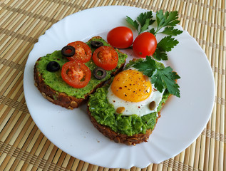 Sandwich with guacamole, egg, olives and tomatoes on a plate