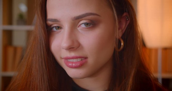 Close-up portrait of cute female student smiles into camera being modest and shy on bookshelves background.