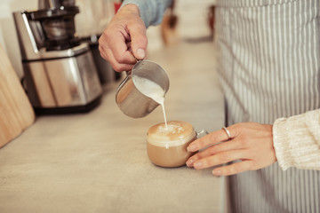 Barista pouring milk into a cup of coffee.