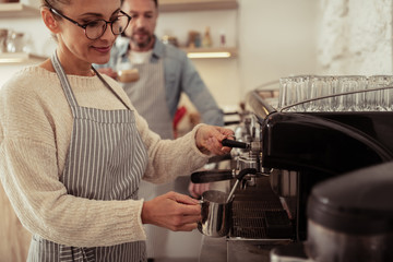 Woman frothing milk by the coffee machine.