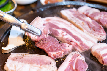 Pan-fried black pork meal in Korea restaurant, fresh delicious korean food cuisine on iron plate with lettuce, close up, copy space, lifestyle