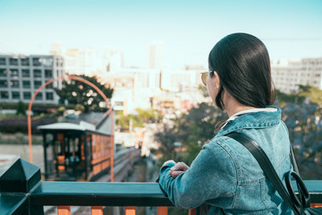 Fototapeta na wymiar back view of young asian girl leaning on rail looking at Angels Flight narrow gauge funicular railway. backpack travelers stand on station located in the Bunker Hill district of downtown Los Angeles.