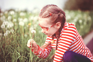 beautiful emotional girl with glasses playing with dandelions. childhood concept