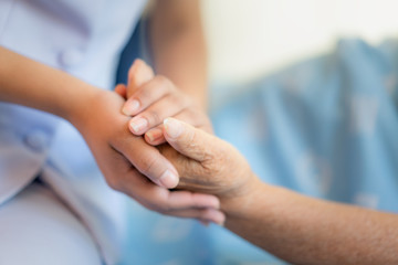 Nurse sitting on a hospital bed next to an older woman helping hands, care for the elderly concept - obrazy, fototapety, plakaty