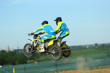 Sidecar motocross athletes jumping on the dirt track 