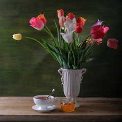 A white cup of tea, a jar of honey and a bouquet of tulips in a vase on the table