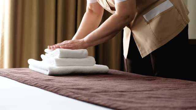 Middle-aged woman's hands beautifully fold white bath sheets of various sizes on the bed of the hotel. The concept of cleaning in the room of a luxury hotel