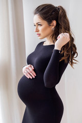 Gorgeous brunette pregnant woman at home in black dress
