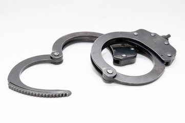 A set of black metal handcuffs with one locked and the other opened on a white background