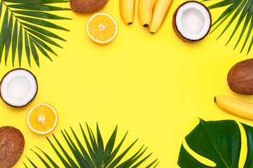 Summer tropical composition. Frame of Green tropical leaves of palm trees and monstera, coconut, orange, bananas on bright yellow background. Flat lay, top view, copy space. Fruit Background