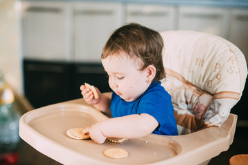 Little girl in a high chair eating round biscuits