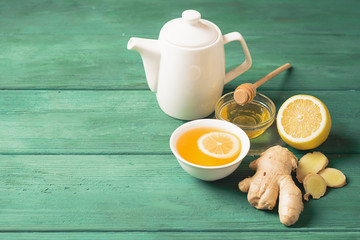 Tea lemon ginger with honey in a white cup and a teapot on a wooden rustic background. Healthy drink for detox health.